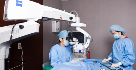 Surgeon and nurse working under a surgical microscope in a Sky Eye Clinic operating room