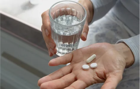 Hand holding two tablets and a glass of water, representing oral medication for non-infectious uveitis